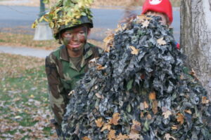A child in camouflage with face paint smiles while playing a hide and seek game outdoors, highlighting the fun and engaging activities in our therapy sessions.